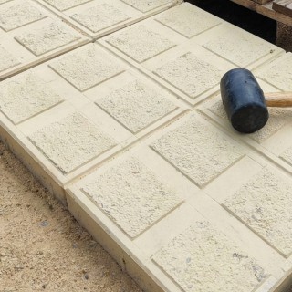 نمای نزدیک نصب کفپوش بتنی طرح مشبک با چکش لاستیکی روی بستر ماسه - سازنده باش (Close-up view of installing grid-pattern concrete pavers with a rubber mallet on a sand bed - Sazandebash)